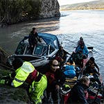 Membres de la GRC, dans un bateau à propulsion hydraulique et sur la rive, aident les gens de deux canots à grimper une pente boueuse