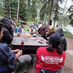 Les participants de l'excursion en canot sont assis autour d'une table de pique-nique du campement et discutent