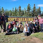 Photo de groupe des participants de l'excursion en canot « Jeunes du Yukon » devant le panneau de Fort Selkirk