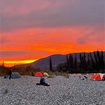 Un coucher de soleil flamboyant et de nombreuses tentes installées le long des rives de gravier