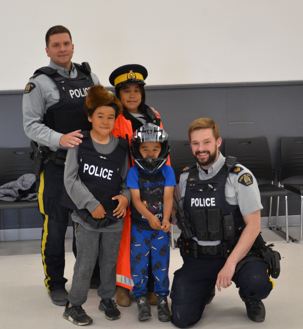 Two RCMP officers with three young kids posing with helmets and police hats
