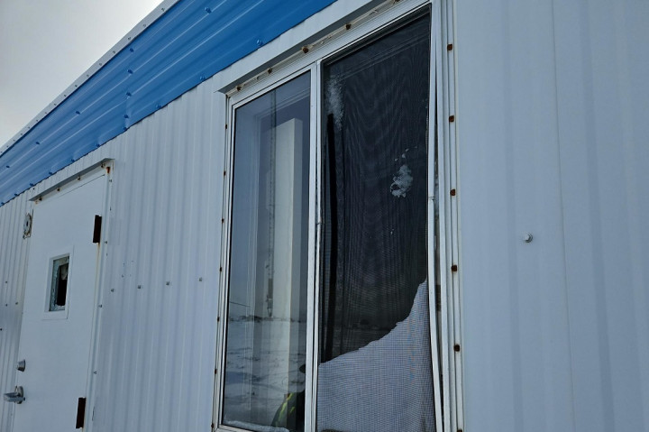 A building is pictured with damages to the glass window pane in a door and damage to another window.