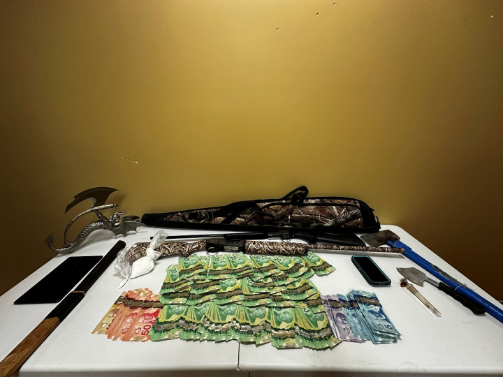 A number of items are displayed on a table, including a quantity of cash, firearms and weapons.