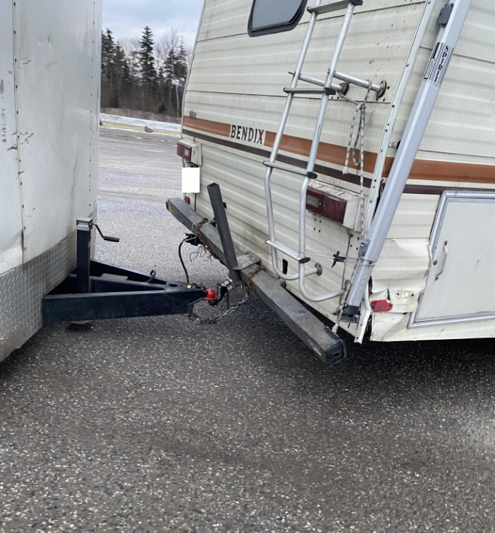 An older motorhome is towing a utility trailer in an unsafe manner. The rear bumper of the motorhome is hanging off the vehicle.