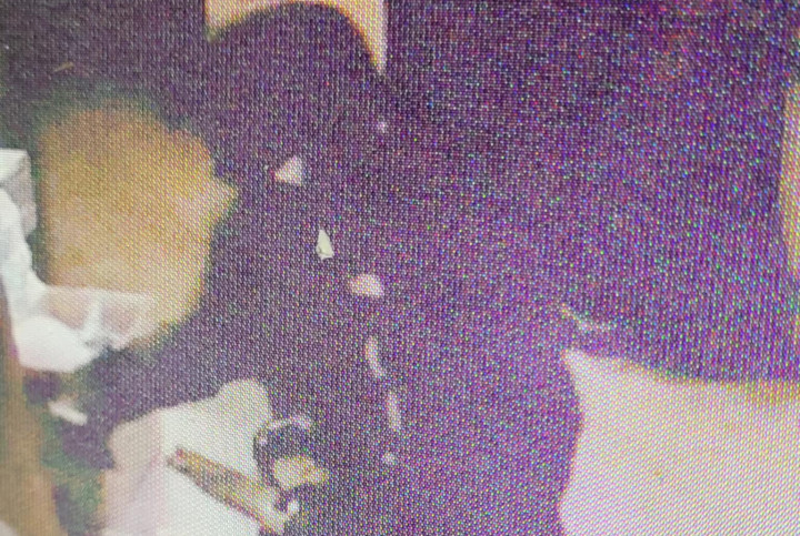 A surveillance image of a suspect wearing dark clothing and holding a shotgun. Their face is covered. 